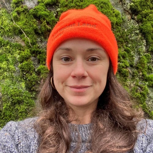 woman wearing orange wool hat standing in front of moss-covered tree trunk_Vermont
