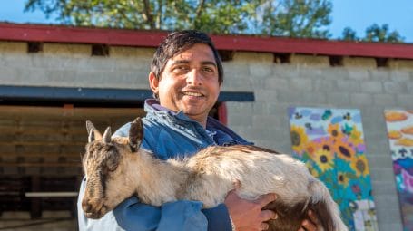 Chuda, a New American farmer at Pine Island Community Farm in Colchester holding a goat