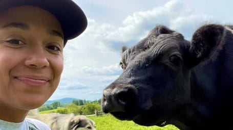 Young woman smiling in close up at camera with a cow and dog nearby