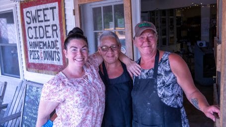 three employees standing in front of the champlain orchards farmstore