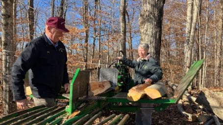 Getting ready for sugaring season, a couple works at wood splitting machine on sunny fall day at Corse Maple Farm