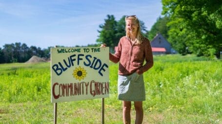 A white woman stands next to a sign reading "Bluffside Community Garden"