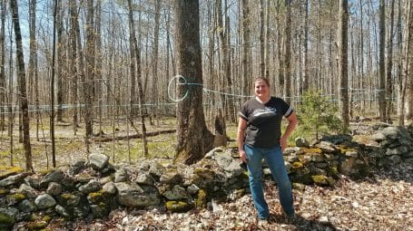 Jessica Boone of Hi Vue Farms standing by old stone wall on her conserved forestland in Vermont