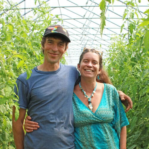 Man and woman in greenhouse with vegetables growing behind them - Evening Song Farm wins 2023 Rozendaal award
