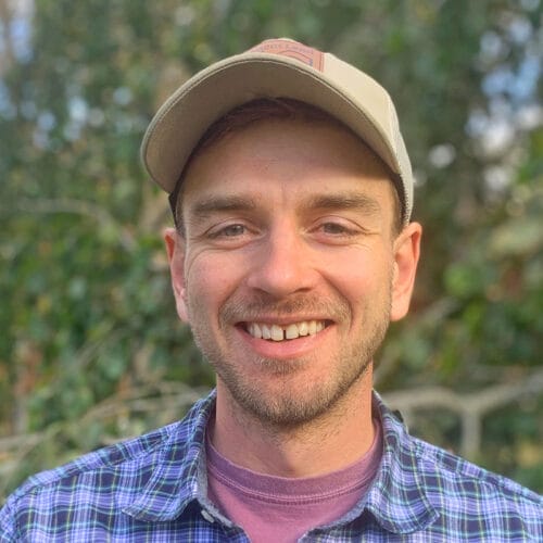 man in baseball cap and checked blue shirt smiling at camera