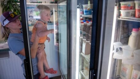 women holding toddler who is eyeing chocolate milk in a cooler at monument farms in weybridge vermont