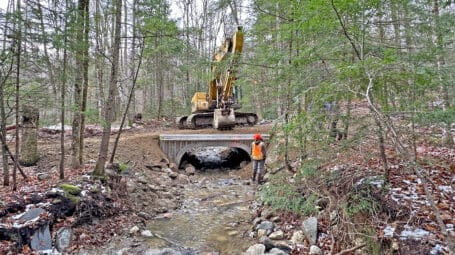 Large excavator on stream-crossing dirt road with newly installed culvert over stream below. Andover Vermont