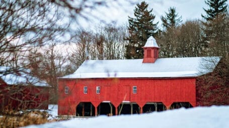 red barn with central cupola in the winter time with snow on the ground - Clemmons family farm in Charlotte Vermont