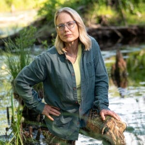 white blond woman wearing glasses standing, with beaver pond in background