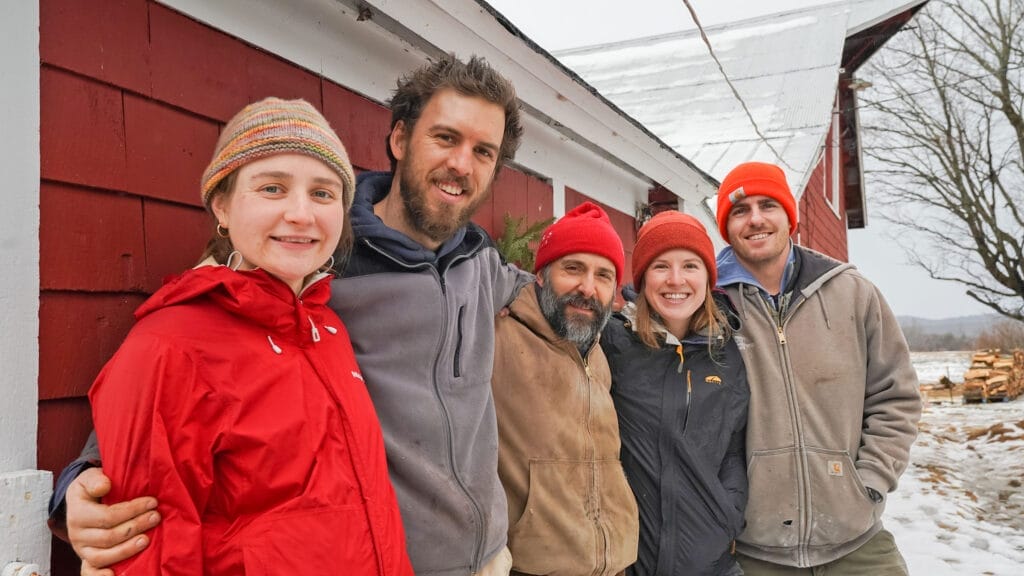 Group of five young farmers standing against red barn in winter - The Farm Upstream - Jericho Vermont - collective