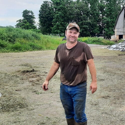 Young male farmer with work-dirtied brown t-shirt and jeans in farmyard. Orwell Vermont 