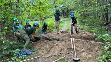 trail crew working on a culvert crossing below a wooded trail with shovels and tools. Brewster Uplands. Vermont