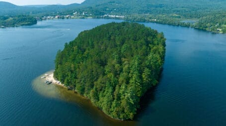 forested island with strip of sandy beach to one side in large lake. Island Pond in Brighton Vermont