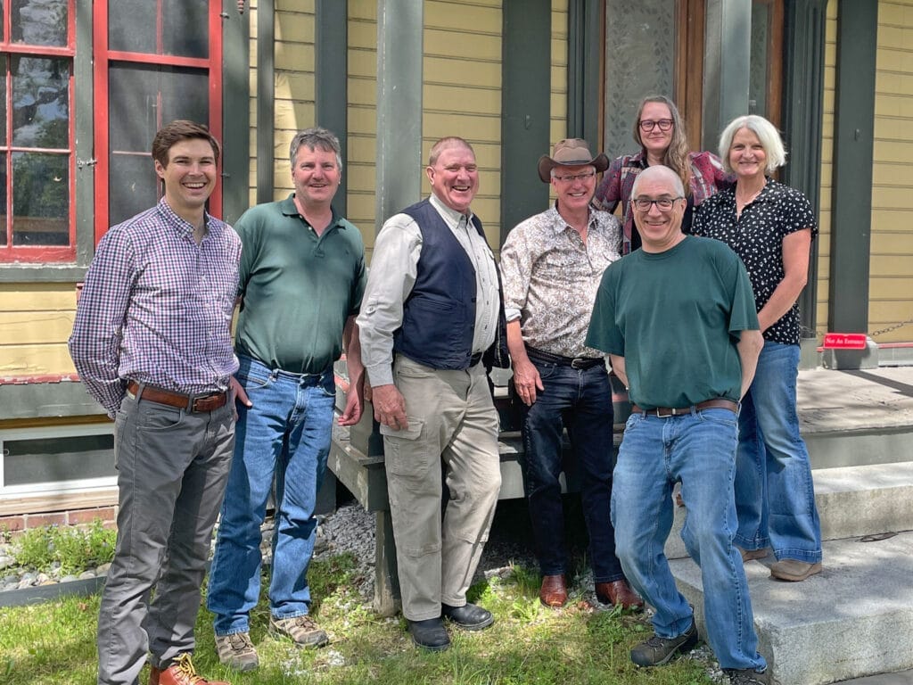 Group of men and woman standing in front of historic building. The team that helped protect the island in Island Pond and add it to Brighton State Park, Vermont.