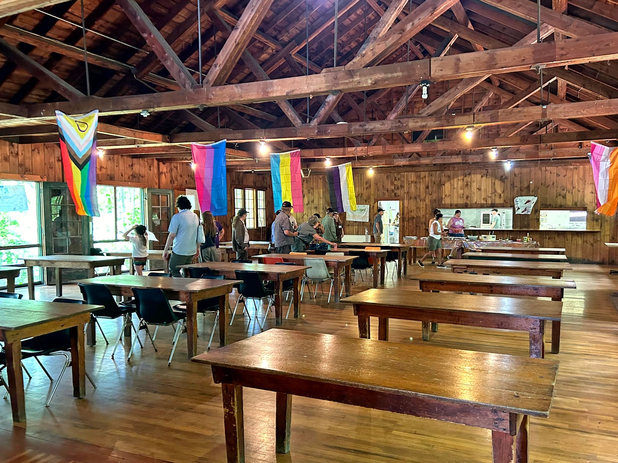 Large timber-framed dining hall with pride flags hanging from rafters