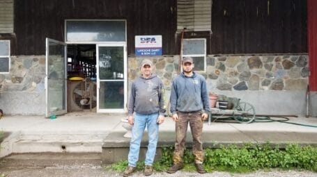 Two white farmers stand in front of the Laroche family dairy business